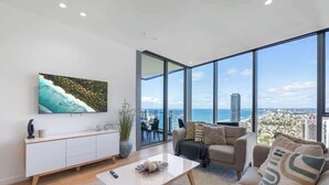 A modern living room with a large window, a white sofa, a coffee table, and a TV on the wall.