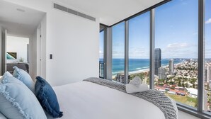 A modern bedroom with a large bed, a view of the city and ocean, and a large window.