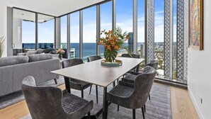 A modern living room with a large dining table, grey sofas, and a view of the ocean.