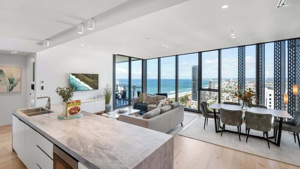 A modern living room with a large window, a kitchen area, and a dining space.