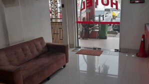 Un'area della reception di un hotel, con un divano, un banco informazioni e una porta in vetro che dà sull'esterno.