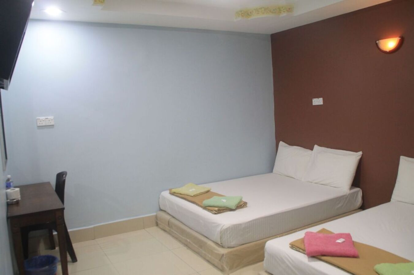 A small, simple room with two beds, a desk, and a chair.