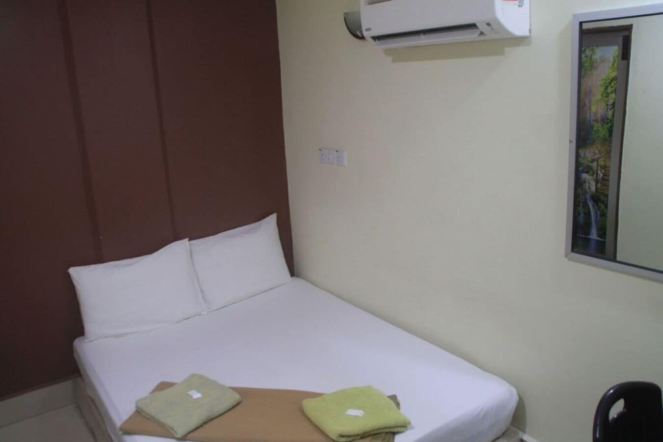 Un lit simple avec du linge de lit blanc, une tête de lit marron et deux serviettes vertes posées au pied du lit.