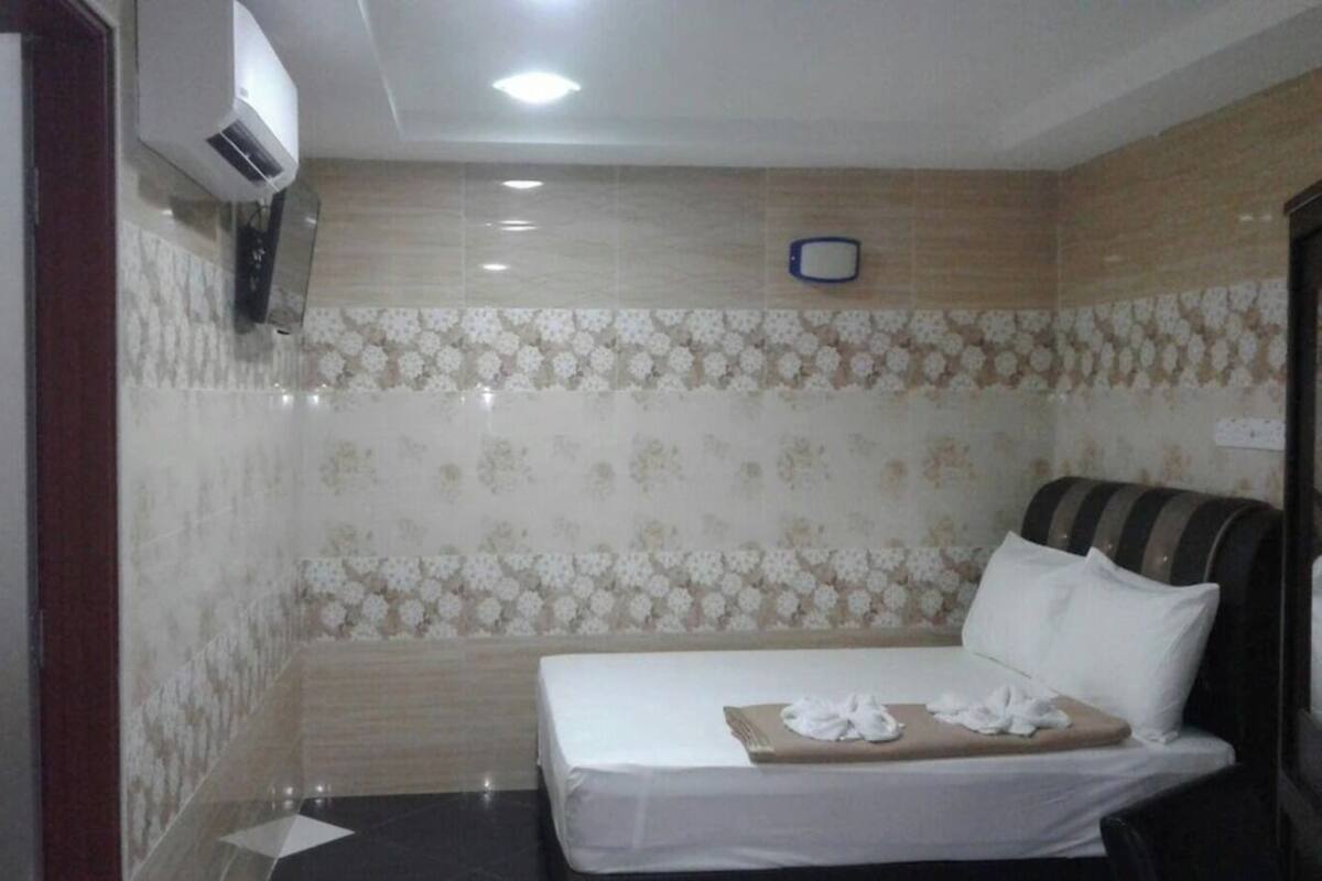 A hotel room with a bed, a TV, and a wall-mounted air conditioner.