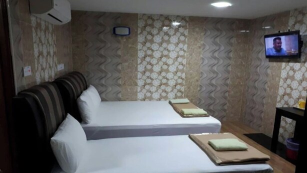 Camera d'albergo con due letti, una televisione e carta da parati decorata.