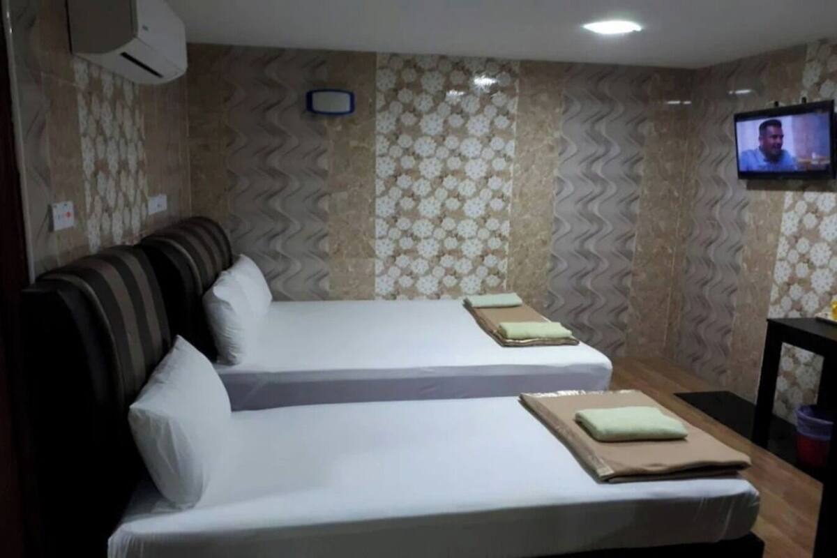 A hotel room with two beds, a television, and patterned wallpaper.