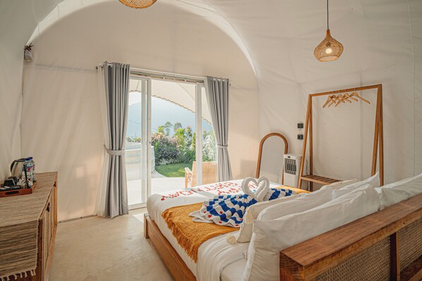 A bedroom with a large bed, a wooden headboard, a bedside table, a mirror, and a view of the outdoors. - Onion Hill Glamping (Kintamani)