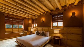 A wooden cabin bedroom with a large bed, two bedside tables, and a window with blinds. - Chulli Bagh Villa  (Leh)