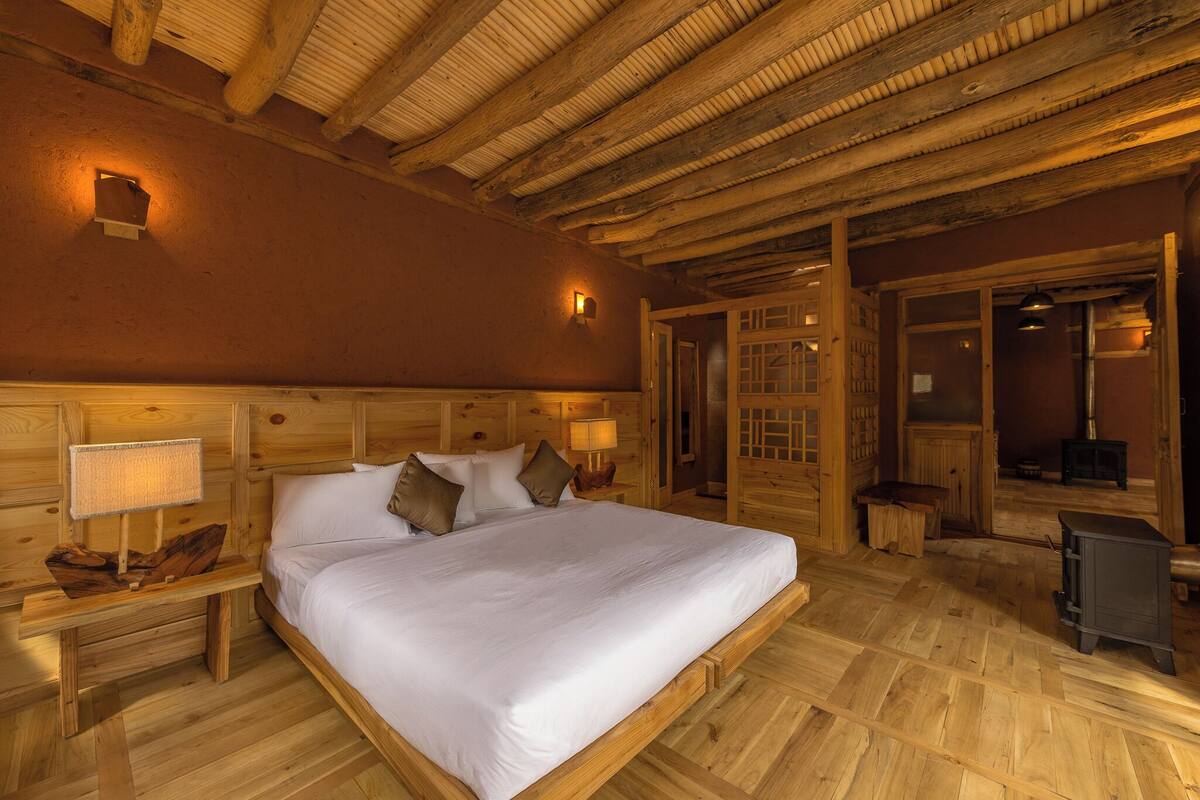 A wooden room with a bed, nightstands, and a fireplace.