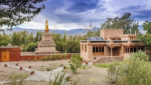 A traditional building with a stupa, surrounded by greenery and mountains in the background. - Chulli Bagh Villa  (Leh)