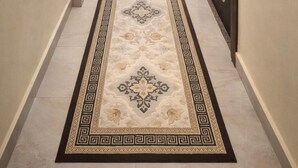 Un corridoio con tappeto decorato, opere d'arte incorniciate alle pareti e una porta con motivo geometrico.