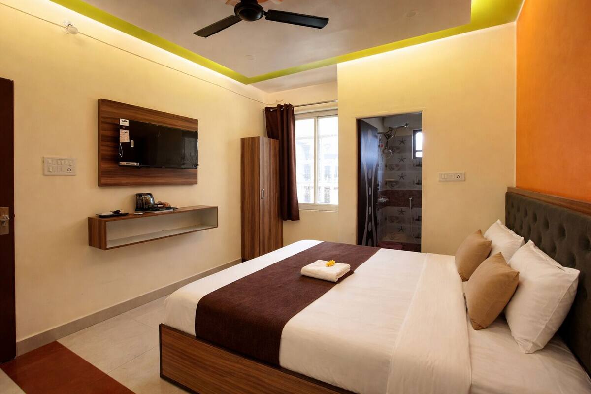 Une chambre d’hôtel moderne équipée d’un lit, d’un téléviseur fixé au mur, d’un espace douche et d’une petite étagère avec des articles de toilette.