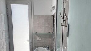 Et badeværelse med en hvid vask, en brusekabine i glas og et flisegulv.