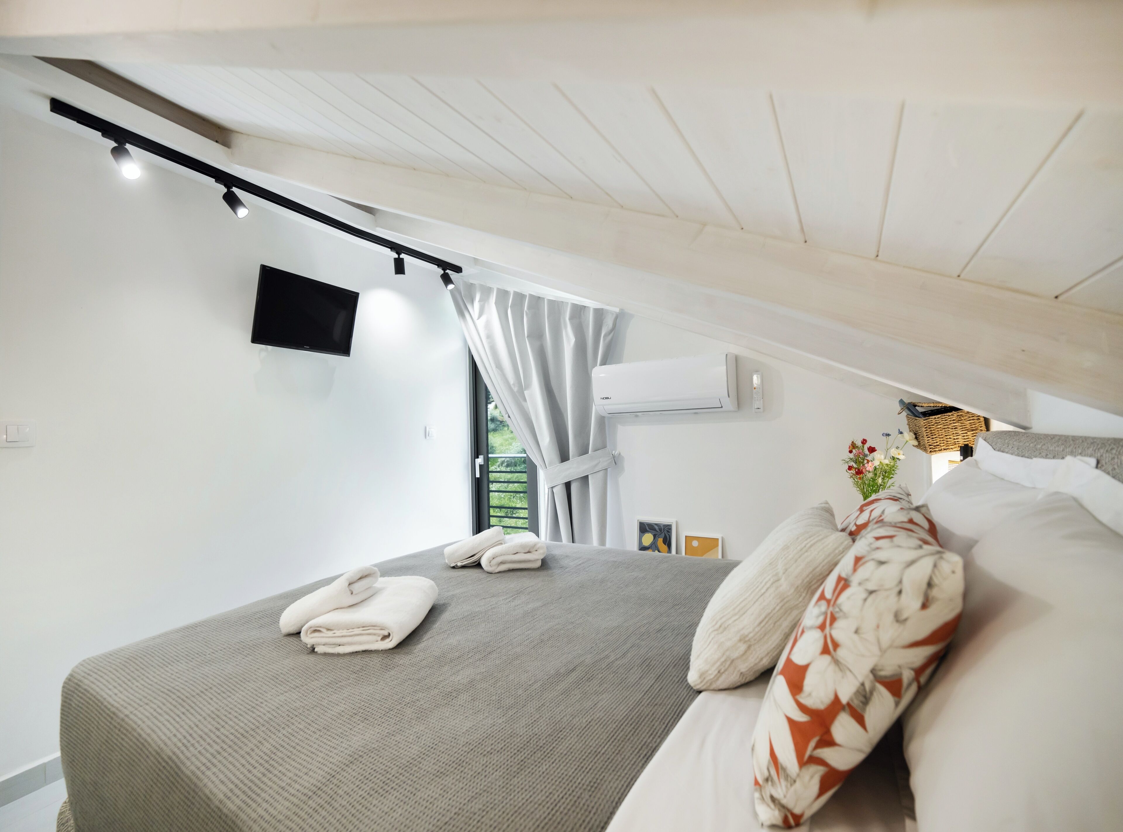 Quarto moderno com cama, televisão de tela plana, aparelho de ar condicionado e janela com cortinas.