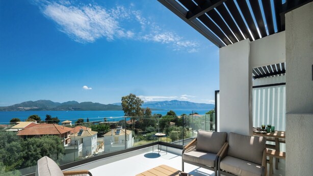 Ein Balkon mit Blick auf das Meer und die Berge, ausgestattet mit einer Couch, Stühlen und einem Tisch.
