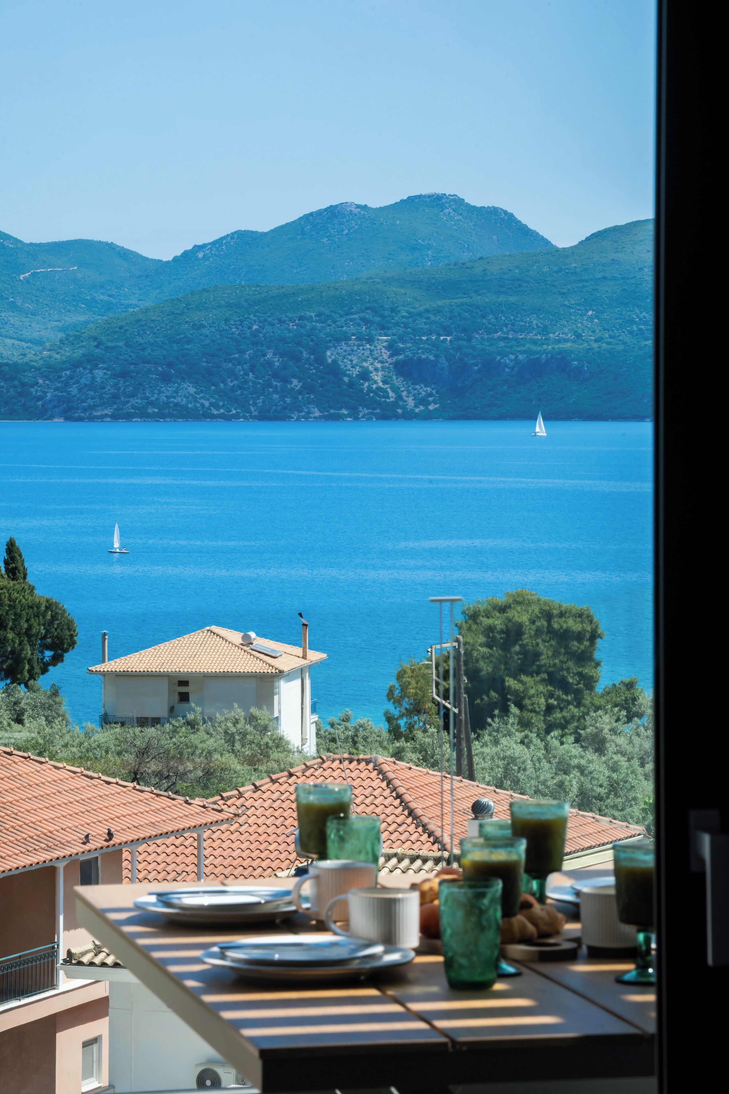 A terrace with a table set for breakfast overlooking a lake with boats, surrounded by hills.