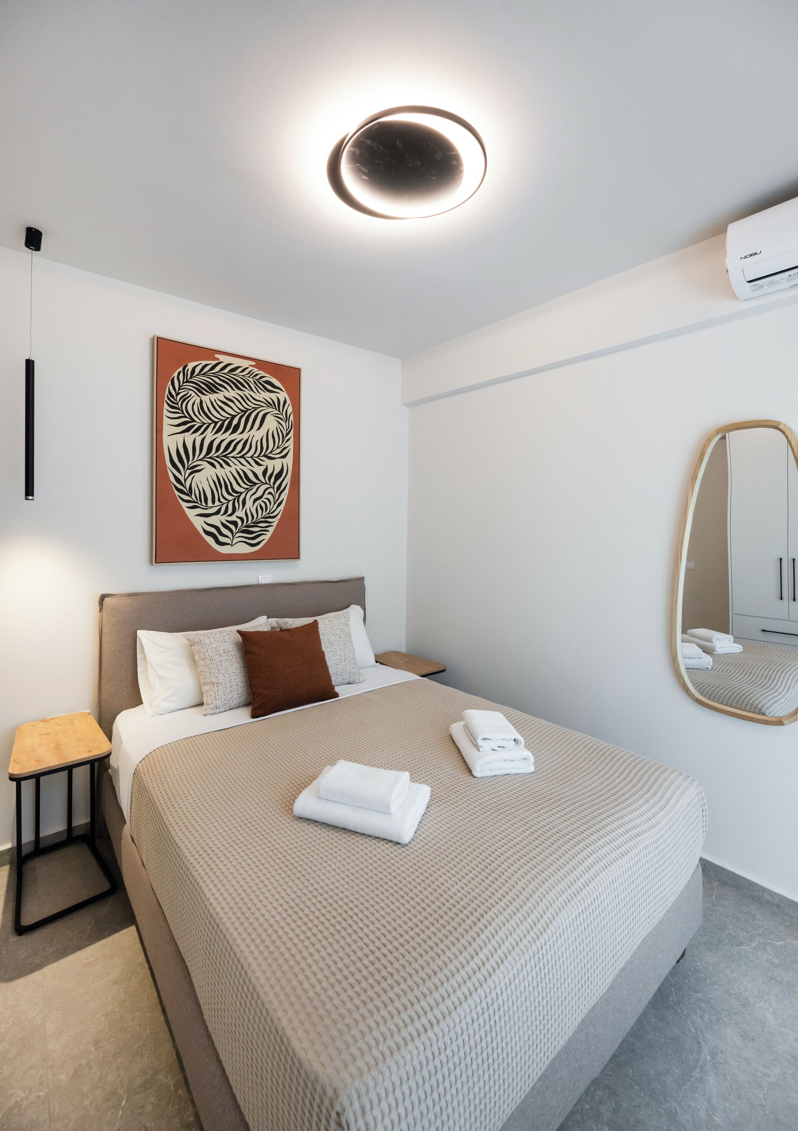 Una habitación de hotel moderna con una cama grande, un espejo fijado a la pared y una lámpara en el techo.