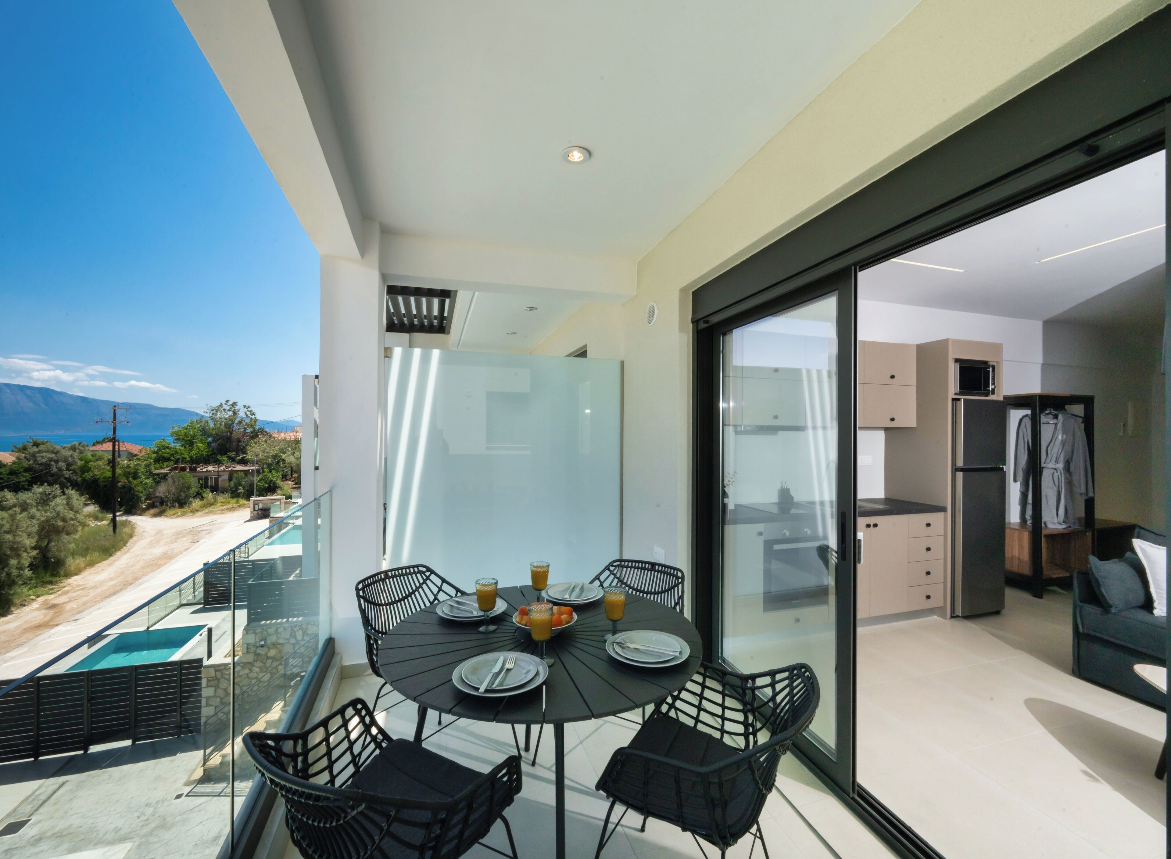 Ein Balkon mit Esstisch und Stühlen, eine Glastür, die zur Küche führt, und Meerblick.