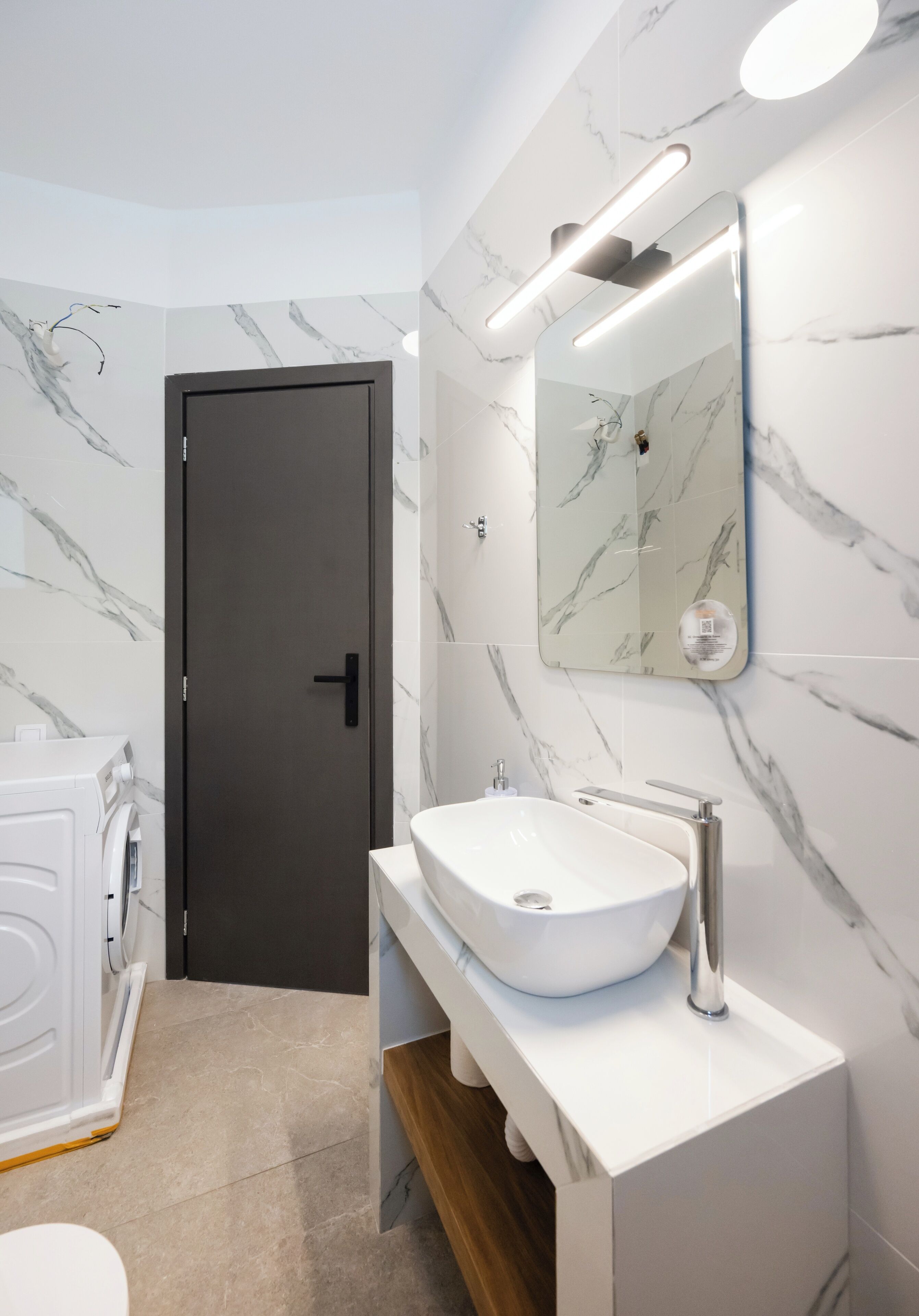 Un bany modern amb paret de marbre, un lavabo blanc i una porta.