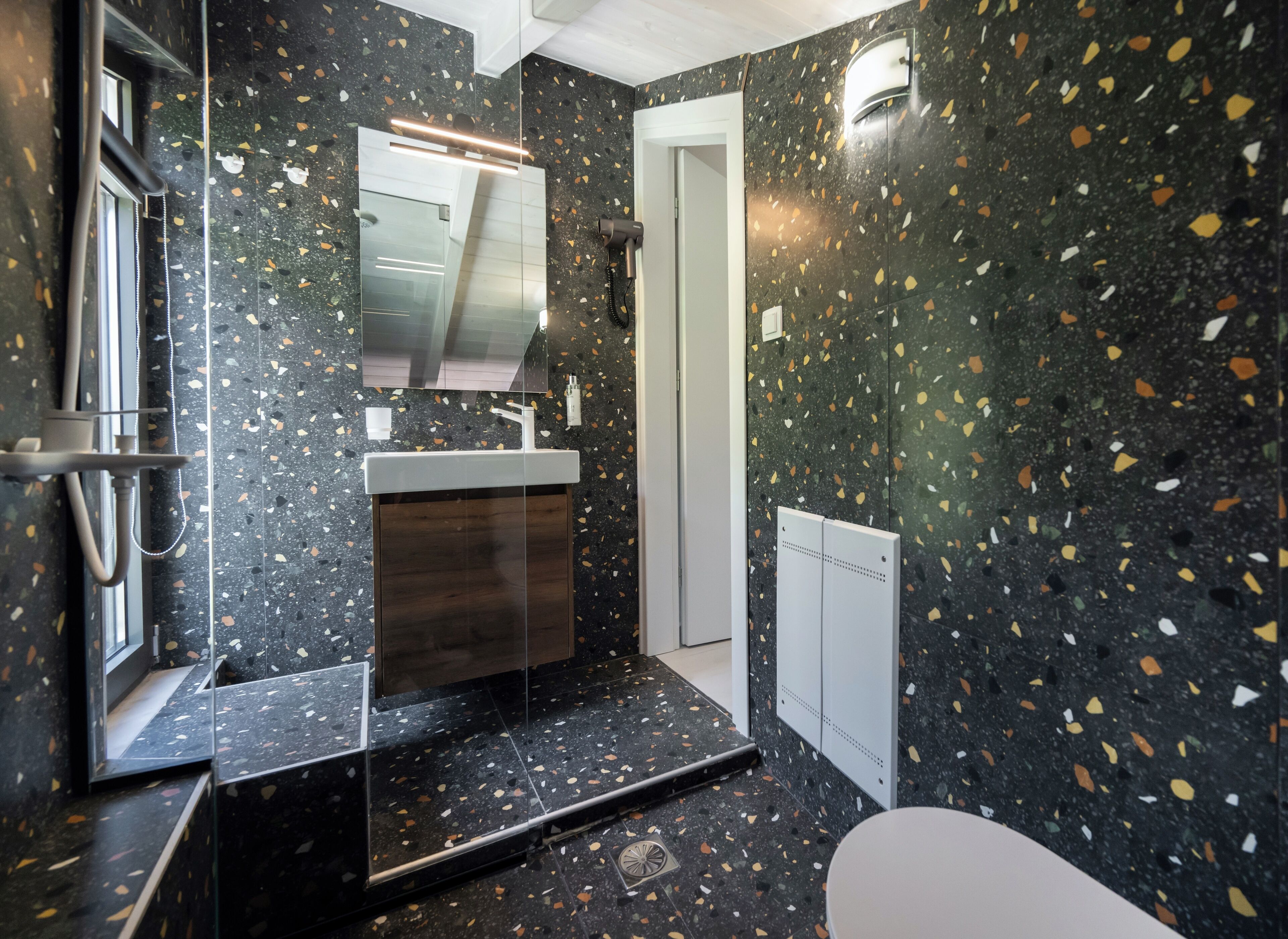 Ein modernes Badezimmer mit dunkel gefleckter Fliesenwand, einem weißen Waschbecken und einem Spiegel darüber.
