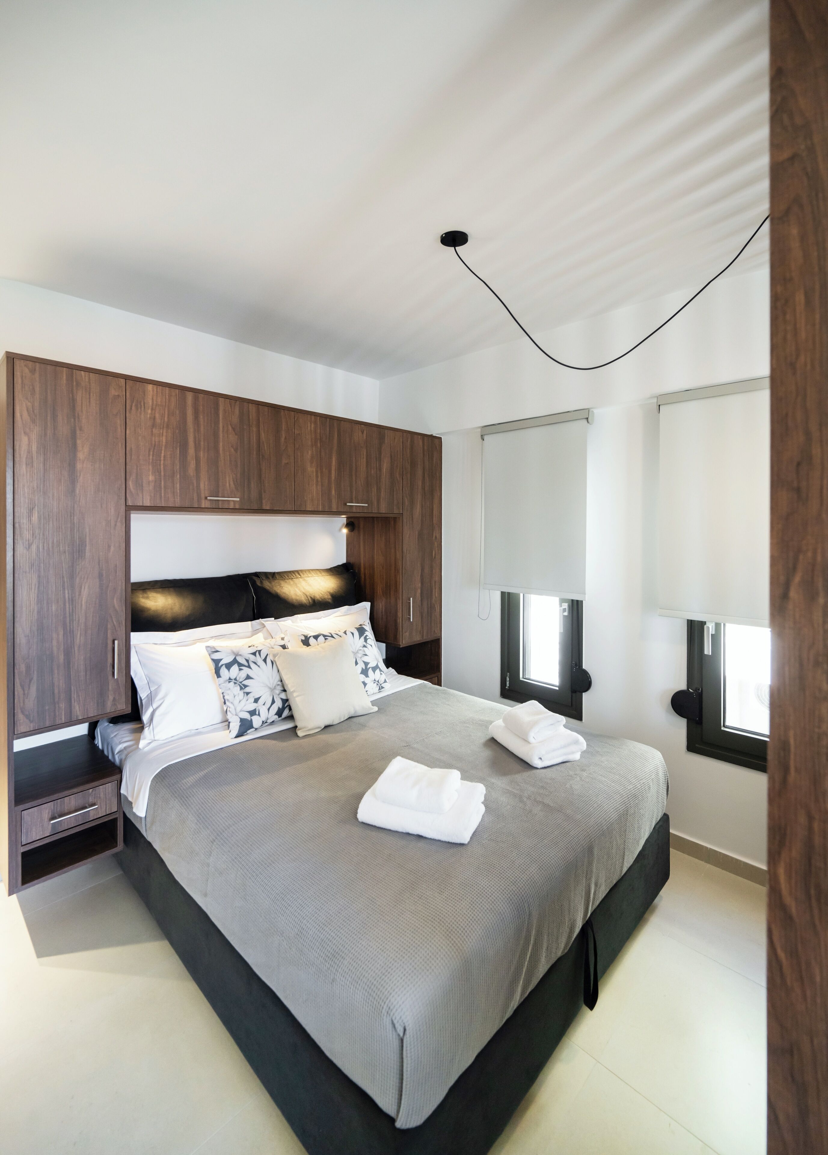 A modern bedroom with a large bed, wooden headboard, bedside tables, and a window with blinds.