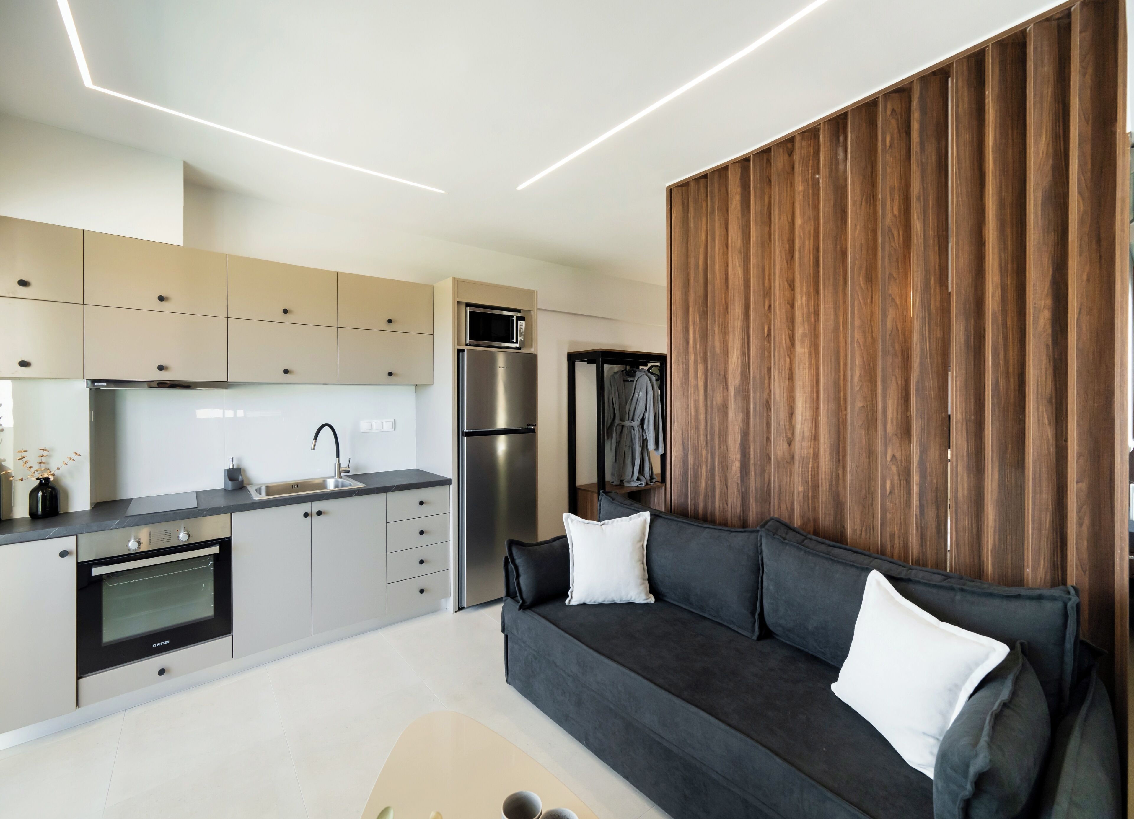 Una cocina moderna con electrodomésticos integrados, un sofá gris oscuro con cojines blancos y un revestimiento de pared de madera.