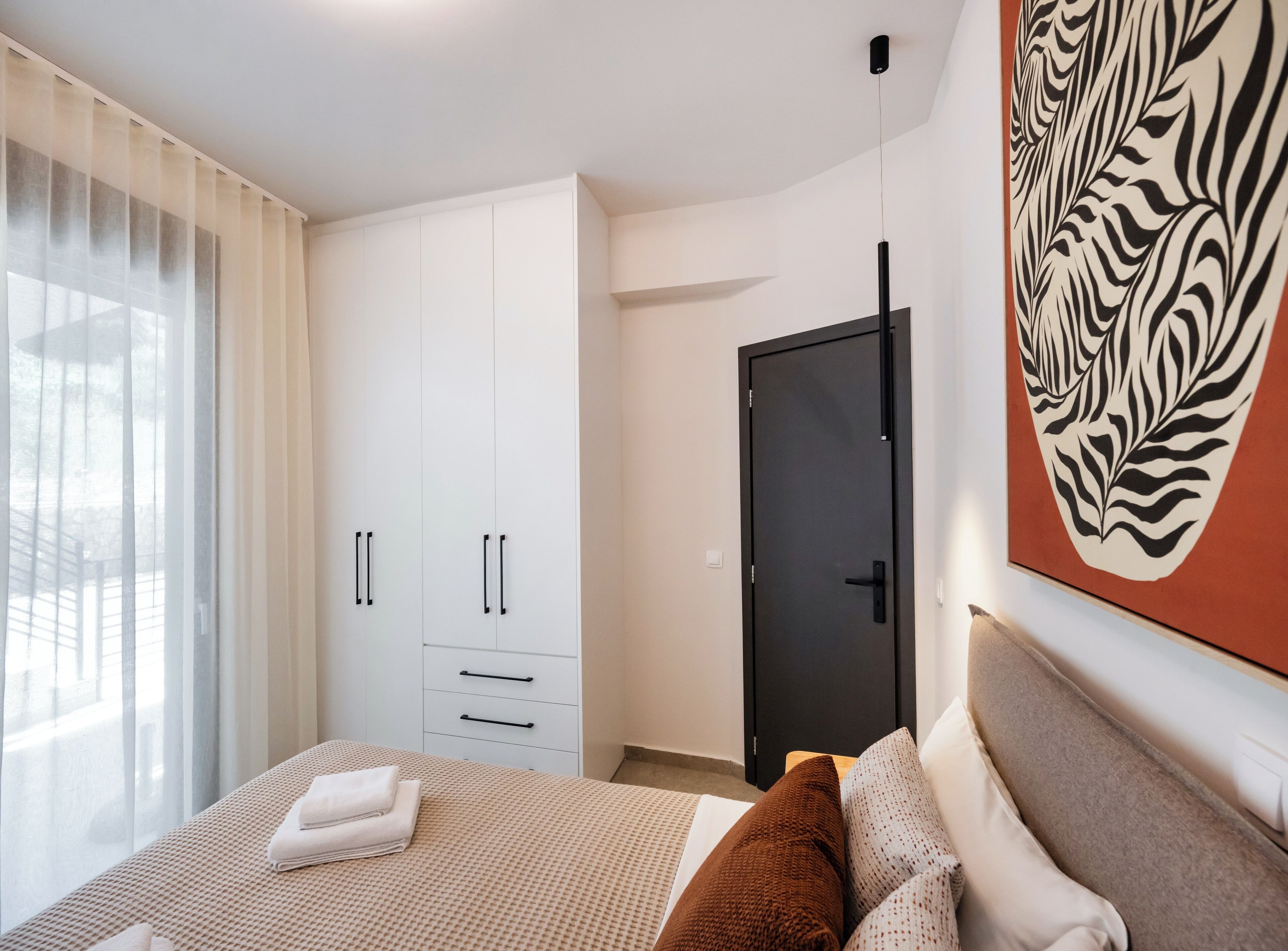 A modern bedroom with a bed, a wardrobe, and a door.