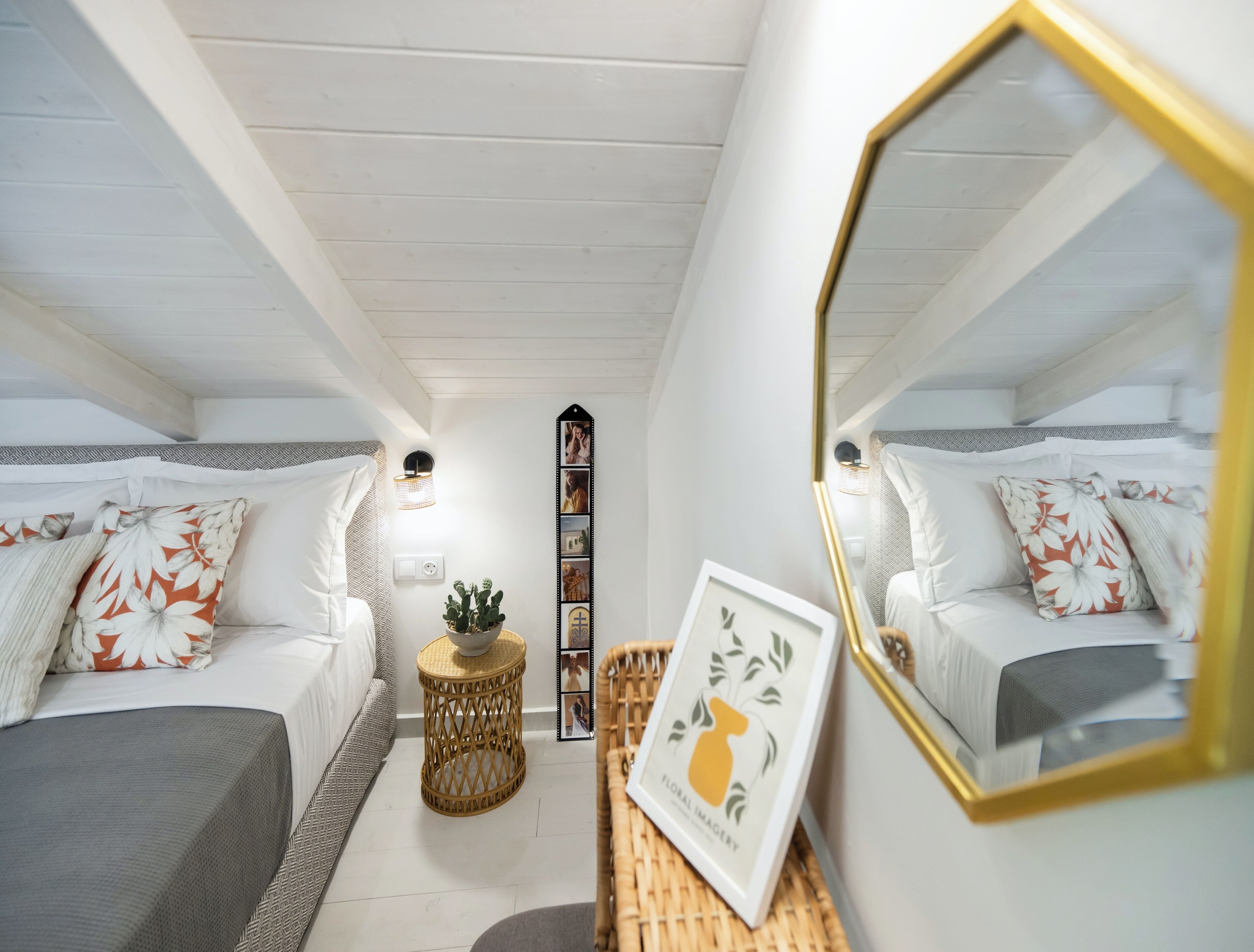A bedroom with two beds, a mirror, a wall-mounted picture frame, and a small side table with a plant.