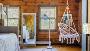A wooden cabin bedroom with a bed, a hanging chair, a floor lamp, and a window with a view of trees. - Pool & Hot Tub, Close to Hiking, Shops & Dining | Cragswood Lodge by AvantStay (Hudson Valley)