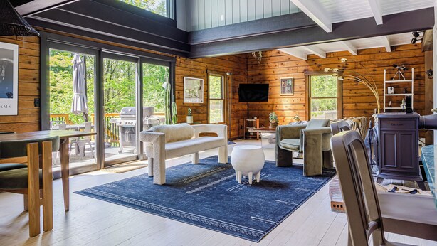 A cozy cabin interior with a large wooden dining table, a sofa, and a fireplace. - Pool & Hot Tub, Close to Hiking, Shops & Dining | Cragswood Lodge by AvantStay (Hudson Valley)