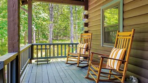 A wooden porch with two rocking chairs and a window overlooking a forest. - Pool & Hot Tub, Close to Hiking, Shops & Dining | Cragswood Lodge by AvantStay (Hudson Valley)