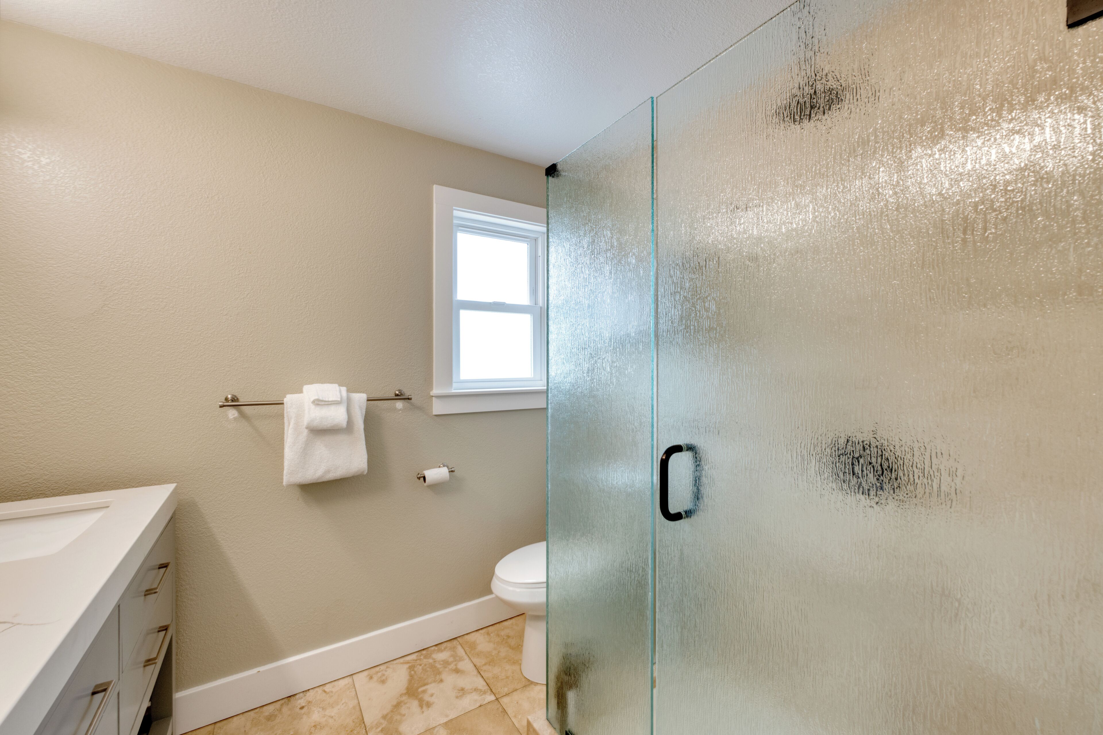 A bathroom with a glass shower door, a white toilet, and a window providing natural light.