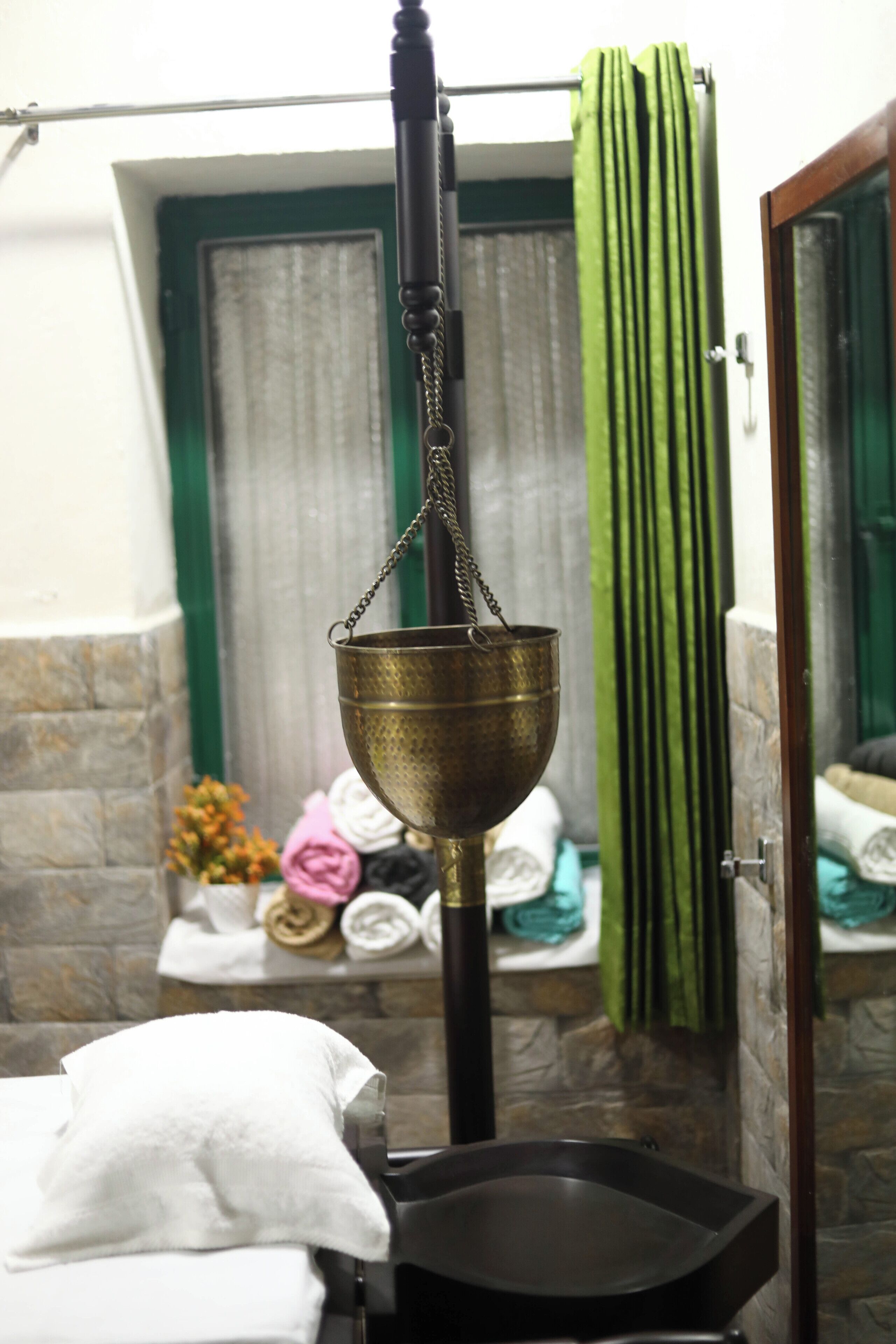 A bathroom with a brass basin, a towel rack with folded towels, and a green curtain.
