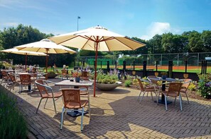 Enjoy a meal under the shade of a large umbrella at Hertog Jan, surrounded by lush greenery and a scenic view.