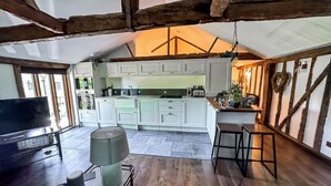 A cozy kitchen with white cabinets, a large window, and a wooden ceiling. - Historic Luxury 18th C Listed Barn Apartment (Maresfield)