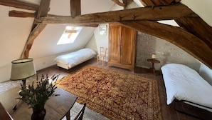 Un dormitorio tipo loft con vigas de madera a la vista, un tapete grande y decorativo, una cama, una silla y una mesita de noche con lámpara.