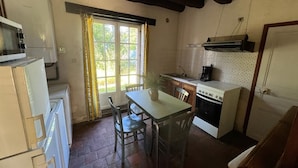 Una cocina compacta con mesa, sillas, refrigerador, estufa y ventana con cortinas.
