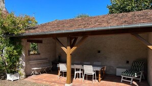 Un patio exterior con una zona de estar techada, una mesa y sillas.