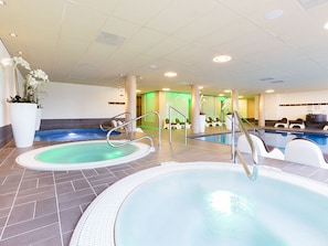 Relax by the indoor pool, featuring two hot tubs with safety railings and a spacious reception area.