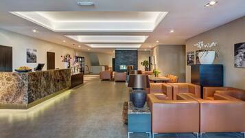 Welcome to our hotel lobby, featuring a central reception desk, comfortable seating area, and beautiful artwork on the walls.