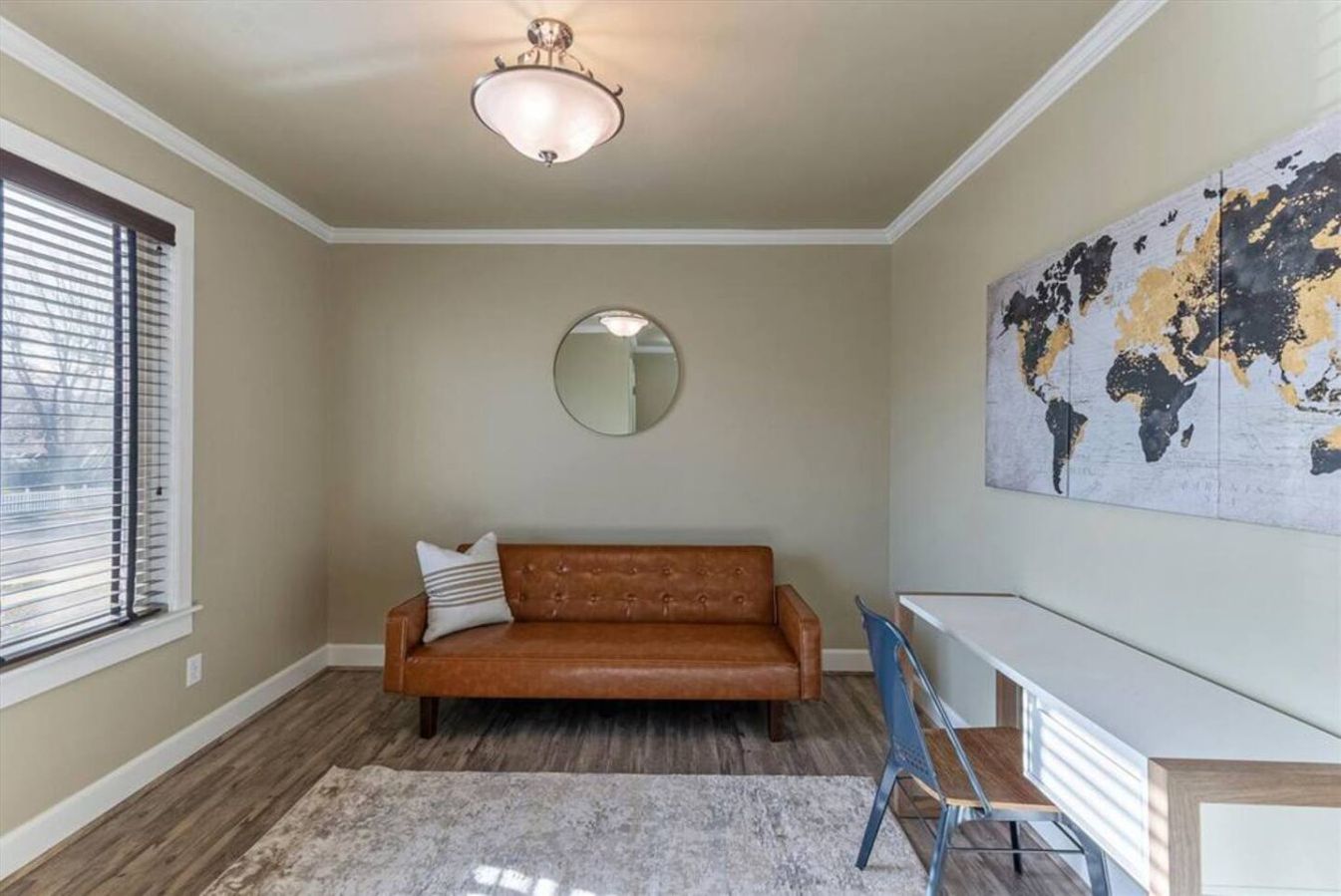 Une pièce avec un canapé en cuir marron, un miroir rond, une carte du monde accrochée au mur, une chaise bleue et un plancher en bois.