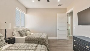 Un dormitorio con dos camas, un aparador, un televisor y una puerta que da a otra habitación.