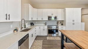 Una cocina moderna con armarios blancos, electrodomésticos de acero inoxidable y una mesa de comedor de madera.