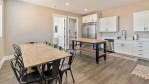 Una cocina moderna con comedor, que cuenta con una gran mesa de madera y sillas, armarios blancos y electrodomésticos de acero inoxidable.