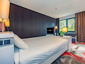 Relax in a spacious room with a large bed, flat-screen TV, and a window with curtains.