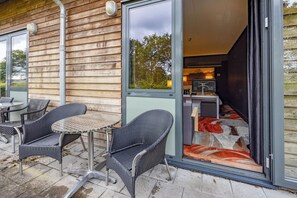 Relax in a serene outdoor space with a round table and two chairs, adjacent to a modern building with a sliding glass door leading to a kitchen or dining area.