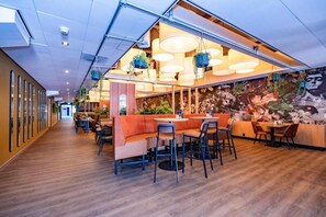 Enjoy dining in a stylish space with a long, narrow layout featuring multiple tables and chairs, a large mural, and pendant lights.