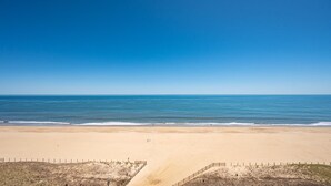 Ein Strand mit blauem Himmel, sandigem Ufer und einer Umzäunung am Rand.