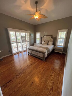 A bedroom with a large bed, a ceiling fan, and a window with blinds.
