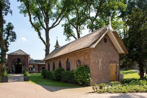 Situated in a serene garden, this traditional chapel features a simple, symmetrical facade with arched windows and a central entrance.